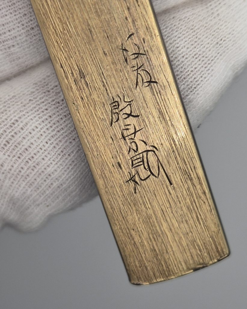 The gold back of the kozuka with the incised signature Goto Injo and kao.