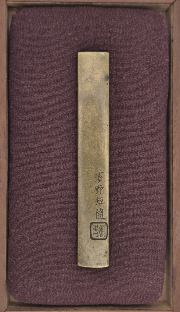 The plain back of the kozuka in its box, signed Hamano Noriyuki with a square seal.