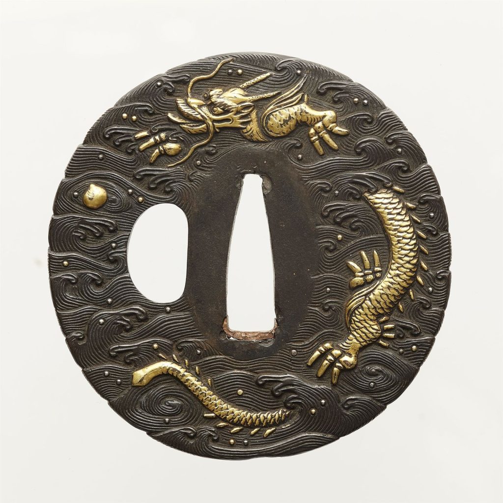 Round shibuichi tsuba covered in finely cut waves: a coiled gold dragon at the top, a small gold jewel floating in the waves beside it.