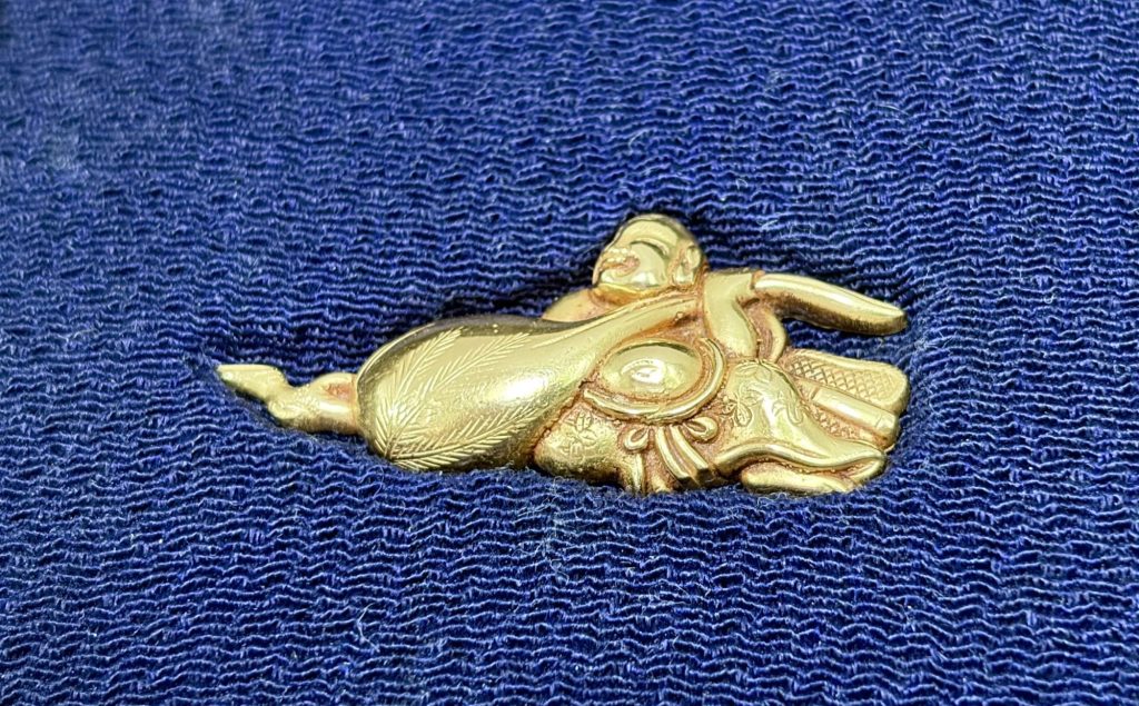 One menuki: Hotei lies smiling behind his bag, one arm thrown wide, the bag engraved with fine lines and tied off at the left.