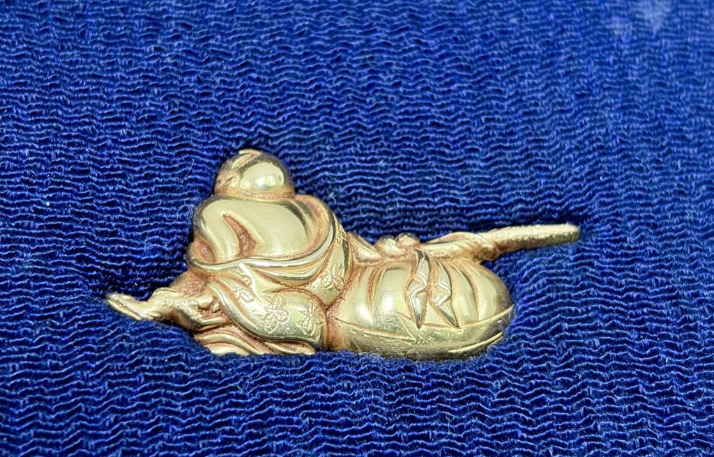 The other menuki: Hotei has sunk forward onto his bag, his bald head bowed, his robe engraved with small flowers.