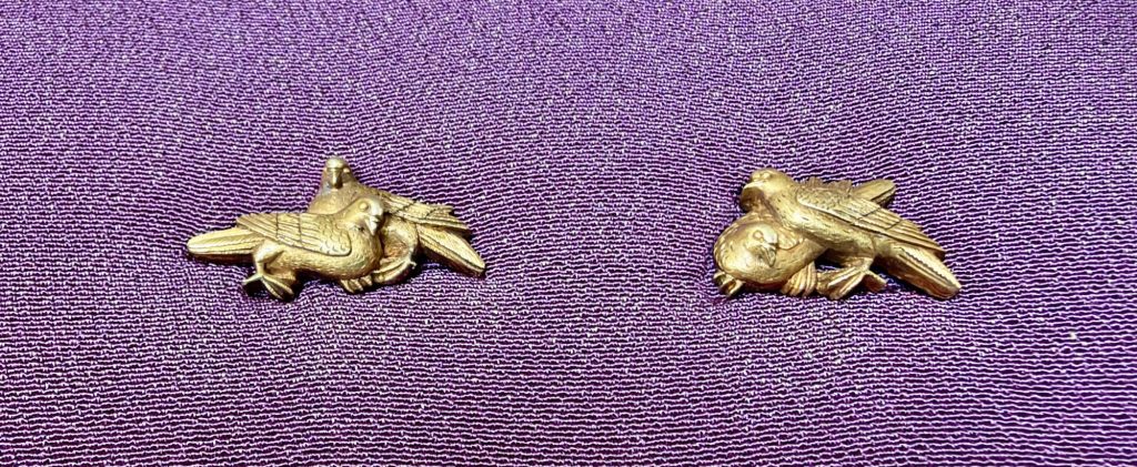 The pair of gold menuki by Ishiguro Masayoshi on purple silk, each with two doves pressed close together.
