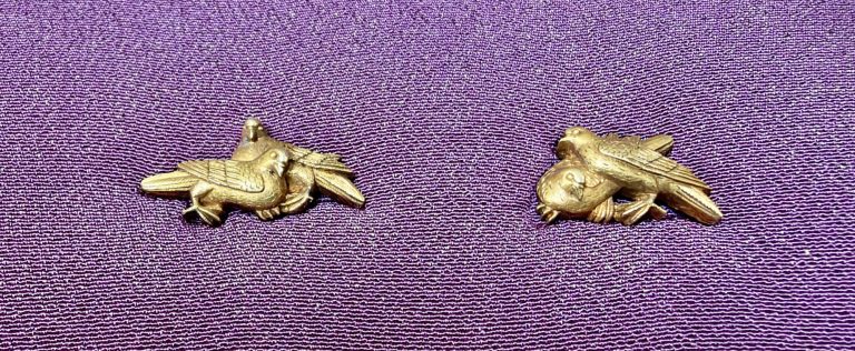 The pair of gold menuki by Ishiguro Masayoshi on purple silk, each with two doves pressed close together.