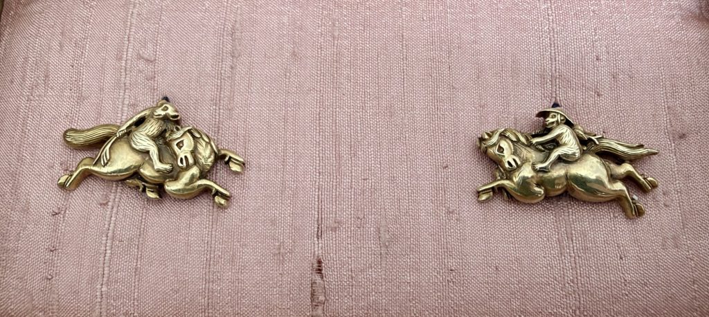 The pair of gold menuki on pale pink silk, each a galloping horse with a monkey on its back.
