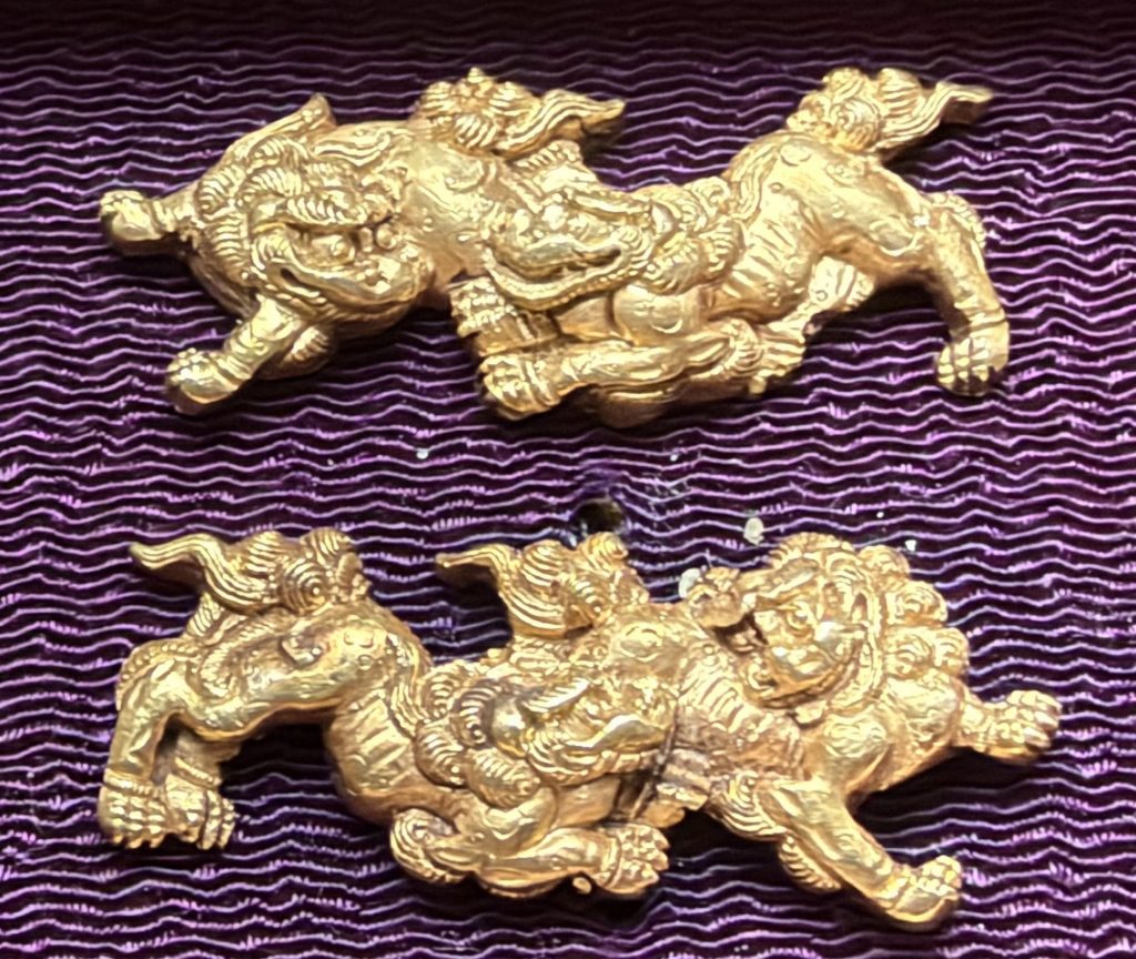 The pair of Kyo-kinko menuki in gold on purple silk, each with two shishi so closely entwined that their heads and paws seem to share one body.