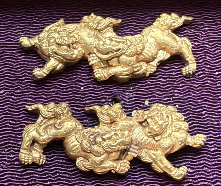 The pair of Kyo-kinko menuki in gold on purple silk, each with two shishi so closely entwined that their heads and paws seem to share one body.