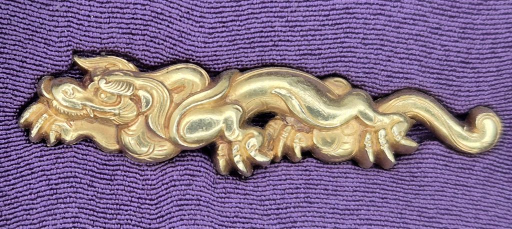 The second dragon of the pair, its head at the left among curling locks of mane, the tail running out to a single curl at the right.