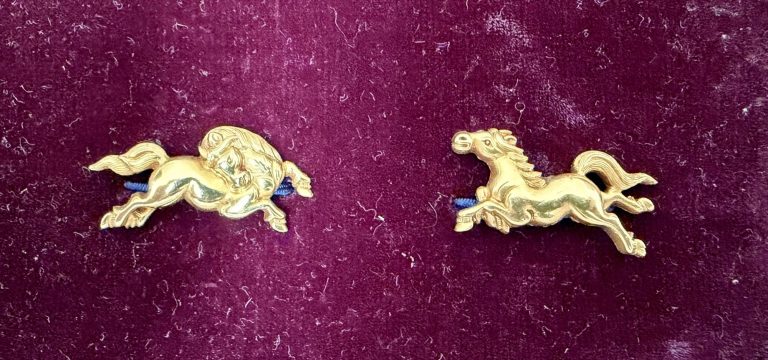 The pair of gold menuki by Yanagawa Naomitsu on deep red velvet, two horses at full gallop running toward each other.