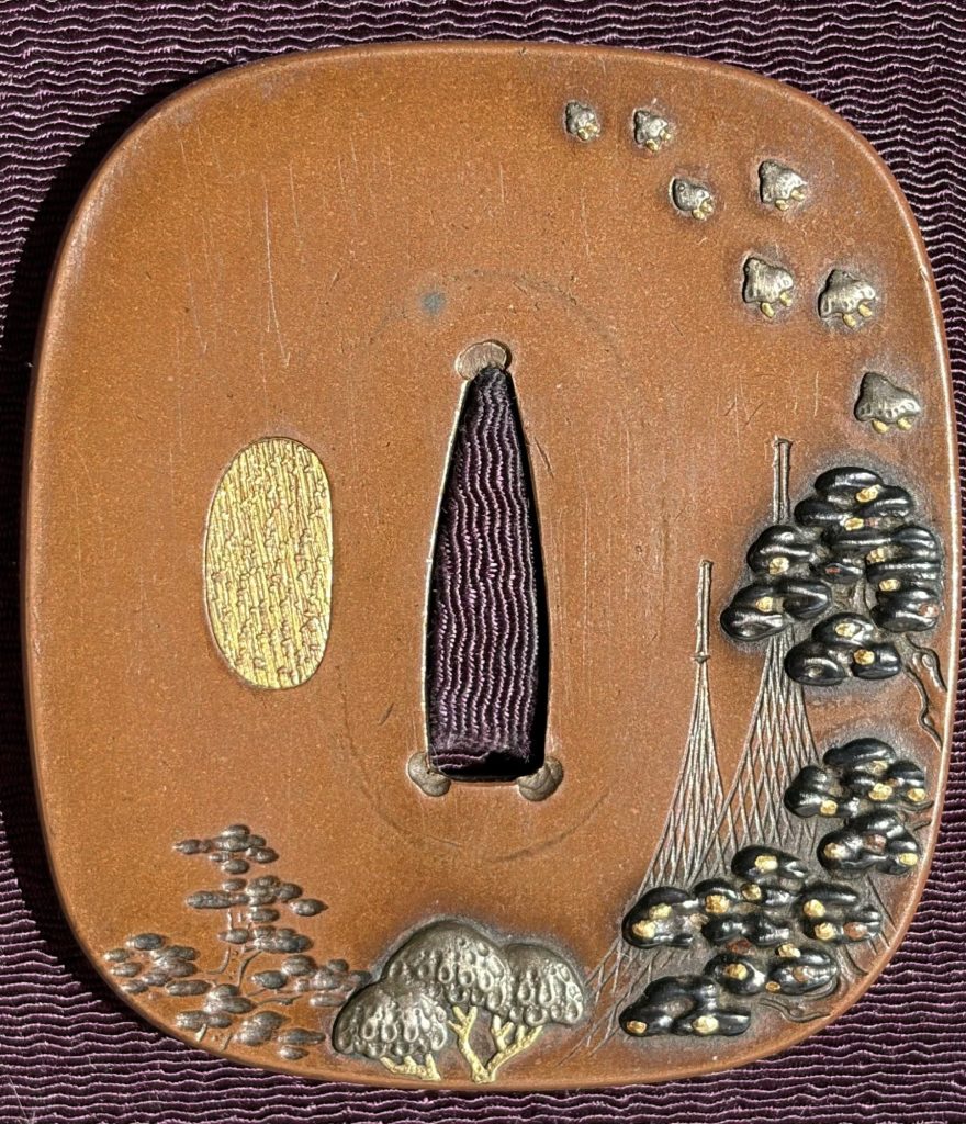 The front of the copper Hamano tsuba: two tall drying nets beside a pine on the right, a flock of plovers above, the hitsu-ana at the left closed with gold.