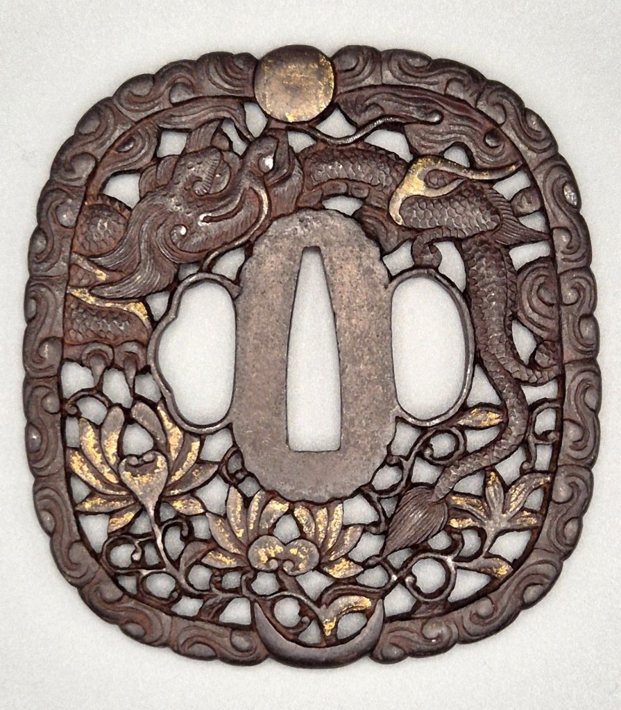 Iron Nanban tsuba in openwork: a scaled dragon arches over the center between a gilded sun at the top of the rim and a crescent moon at the bottom; lotus flowers touched with gold fill the lower half.