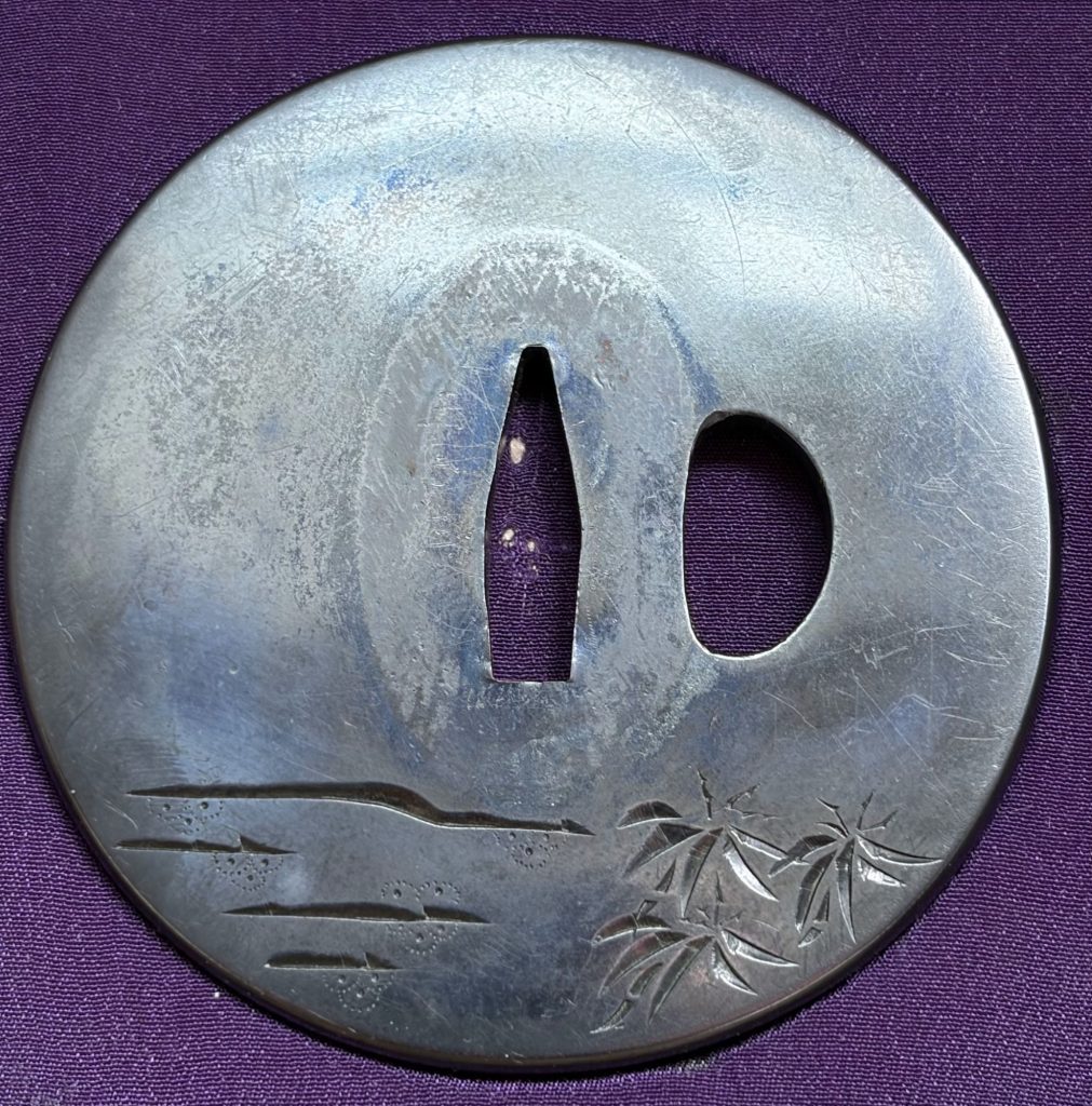 The back of the tsuba, left almost empty, with a few long strokes of water at the lower left and a spray of bamboo at the lower right.