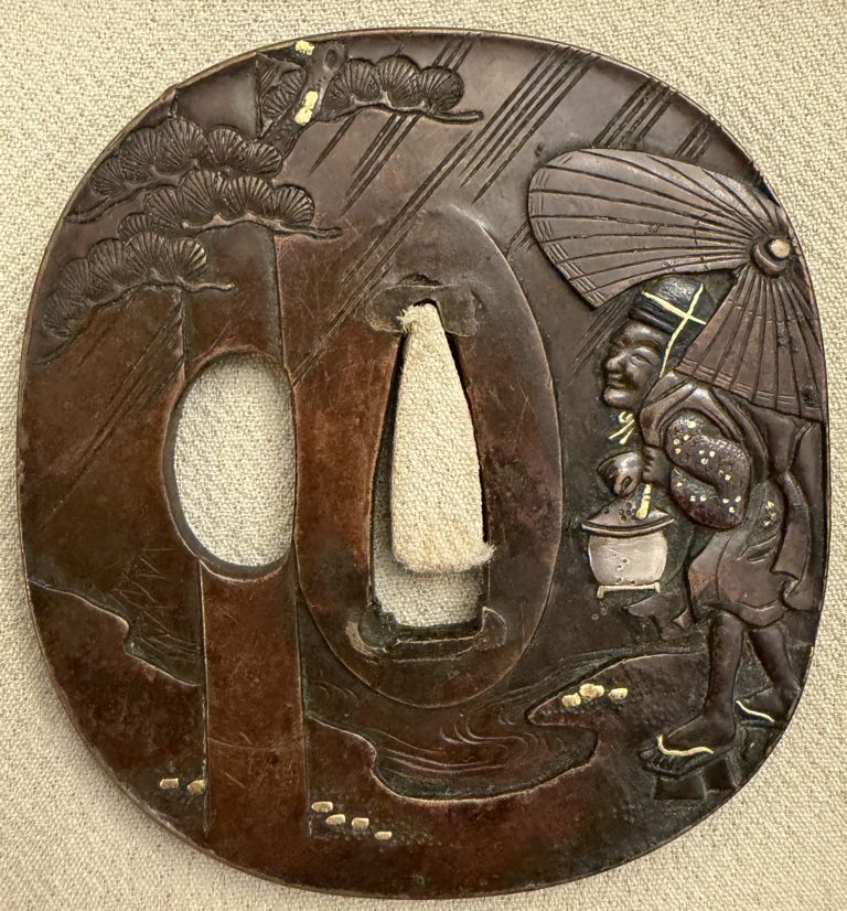 Aridoshi tsuba in sentoku under a reddish patina: an old man in a black cap walks through slanting rain under a large paper umbrella, a lantern in his hand; at the left an upright post rises past a pine.