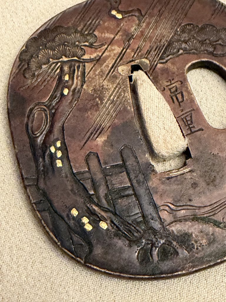 Detail of the back: the pine trunk touched with gold, the fence below, rain across the plate and the two characters of the signature.