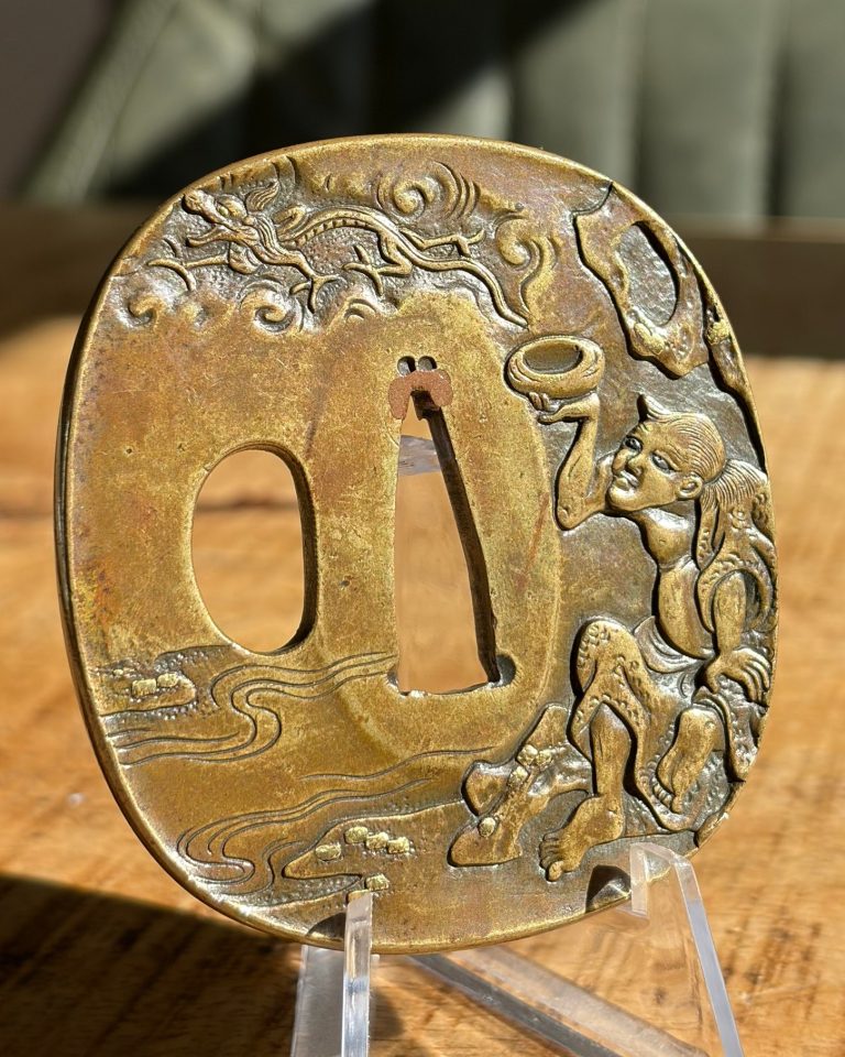 Tsuba by Tsuneshige: a seated figure lifts a bowl while a dragon moves through clouds along the upper edge.