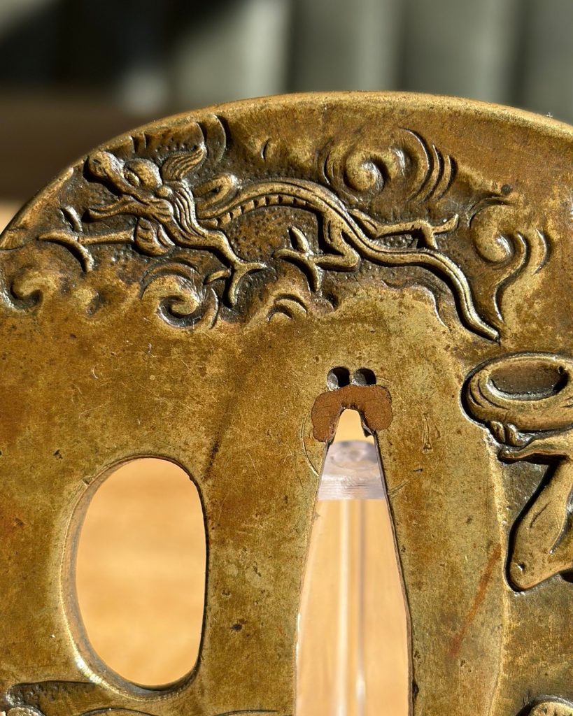 Detail of the dragon in low relief among scrolling clouds above the blade opening.