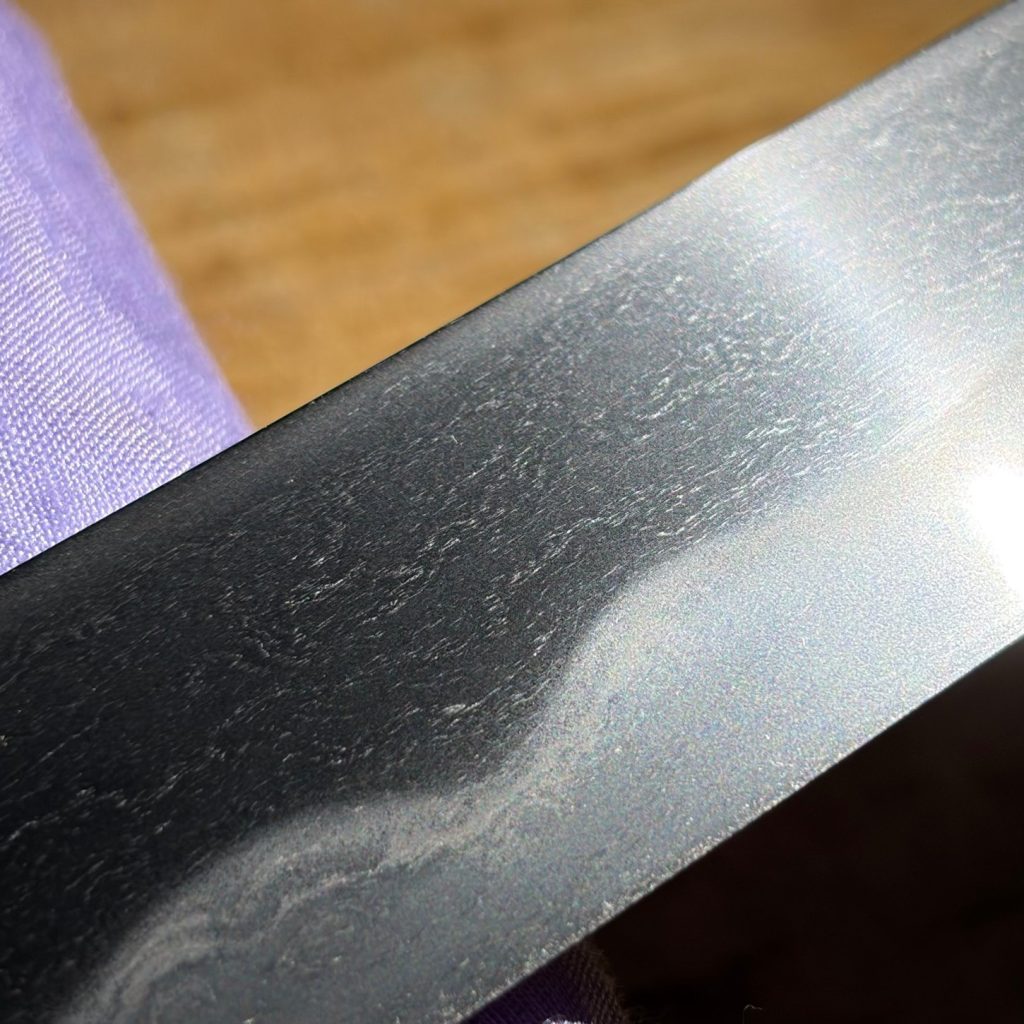 Close view of the blade: itame grain with mokume rings above a soft notare hamon.