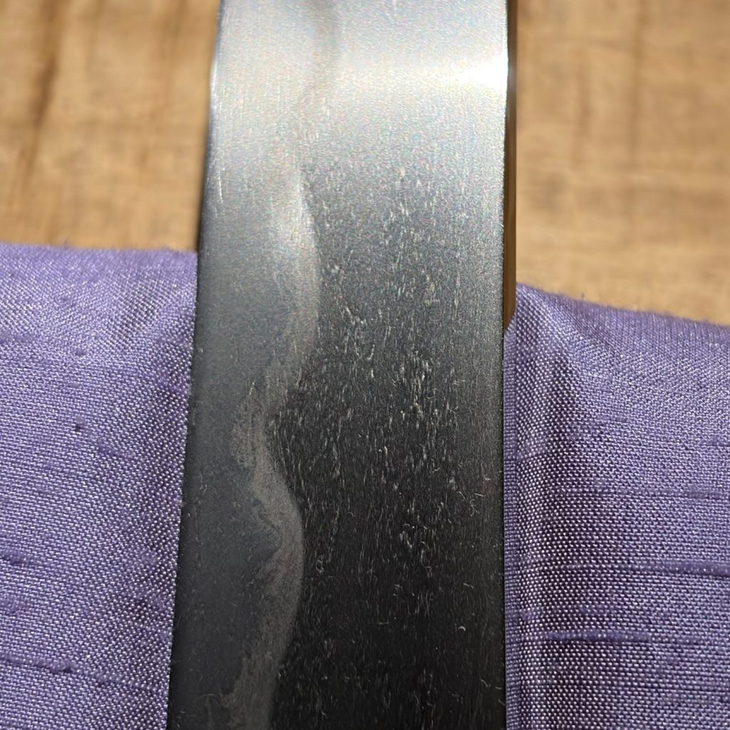 The middle of the blade: a broad notare hamon over dark, open grain.